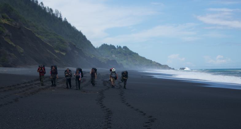 Trekkers framed by the beach cliffs and tide. Photo by Spencer Cross.